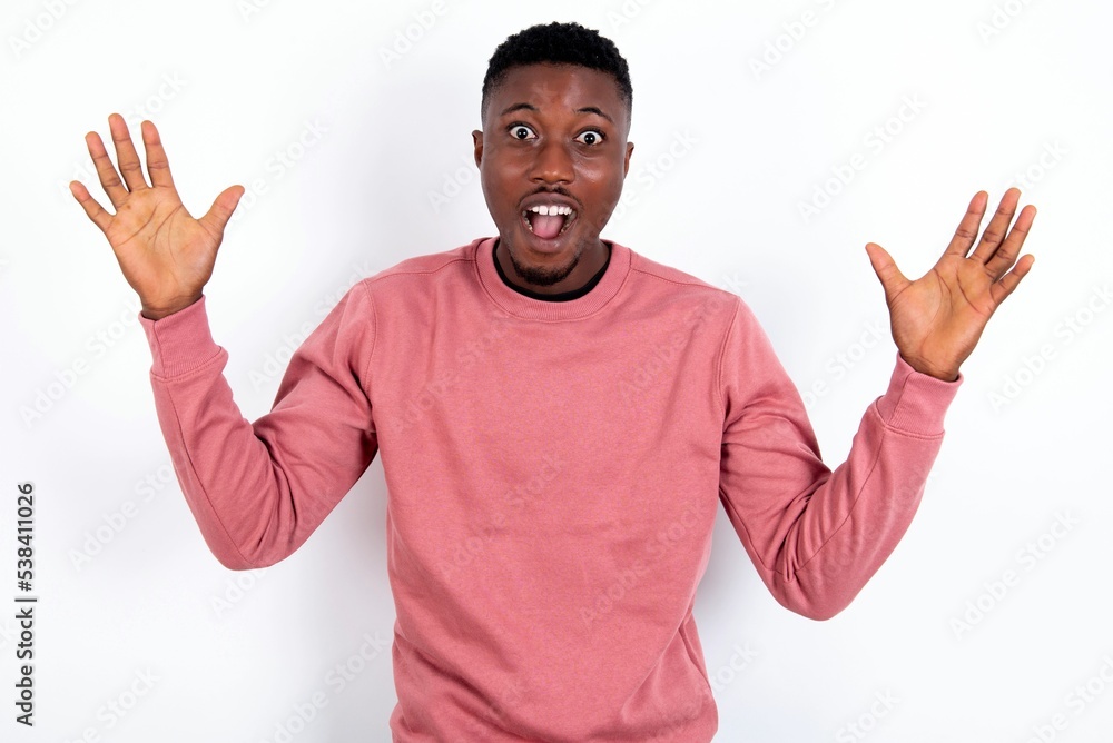 young handsome man wearing pink sweater over white background raising hands up, having eyes full of happiness rejoicing his great achievements. Achievement, success concept. young handsome man wearing pink sweater over white background raising hands up, having eyes full of happiness rejoicing his great achievements. Achievement, success concept.