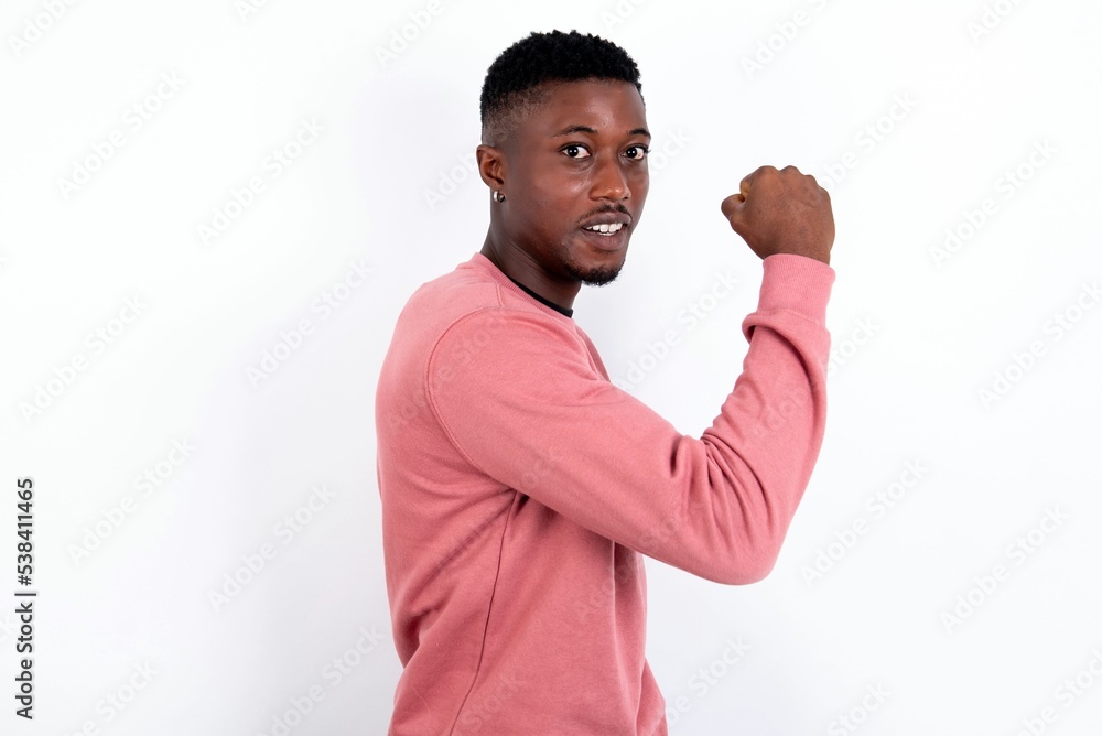 young handsome man wearing pink sweater over white background, showing muscles after workout. Health and strength concept. young handsome man wearing pink sweater over white background, showing muscles after workout. Health and strength concept.