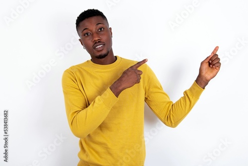 Positive young handsome man wearing yellow sweater over white background with beaming smile pointing with two fingers and looking on empty copy space. Advertisement concept.