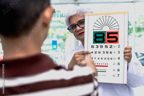 Old Indian optician woman showing snellen eye testing chart to boy paitent in optical clinic, Ophthalmologist Glasses Concept photo