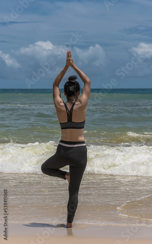 Sporty sexy woman standing with one leg doing tree pose yoga on beach, Yoga Concept