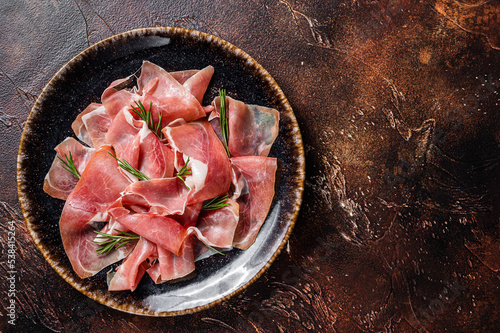 Slices of prosciutto crudo parma or jamon serrano with rosemary. Dark background. Top view. Copy space
