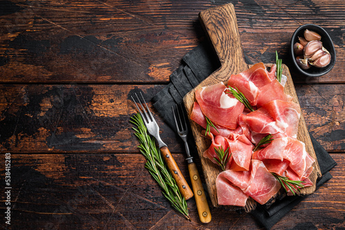 Slices of jamon serrano ham or prosciutto crudo parma on wooden board with rosemary. Wooden background. Top view. Copy space