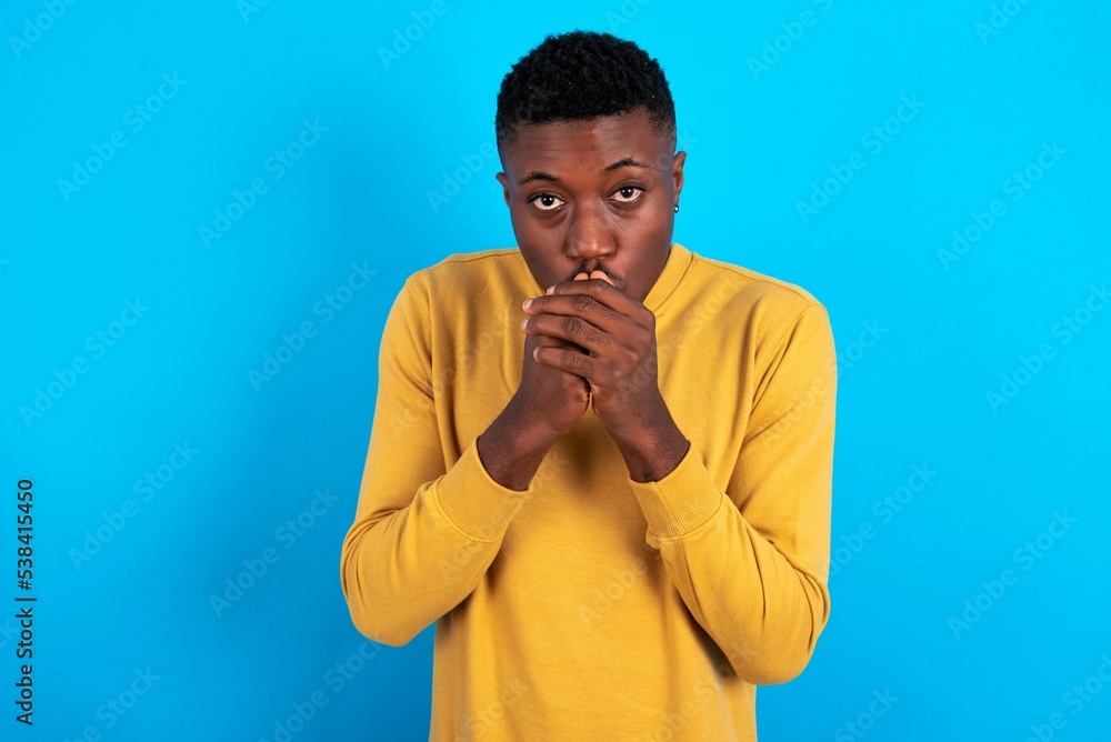 young handsome man wearing yellow T-shirt over blue background holding oneself, feels very cold outside, hopes that will not get cold young handsome man wearing yellow T-shirt over blue background holding oneself, feels very cold outside, hopes that will not get cold