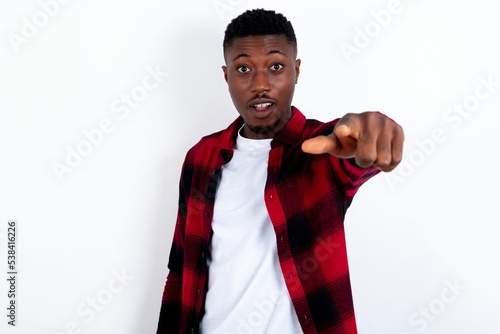 Excited positive young handsome man wearing plaid red overshirt over white background points index finger directly at you, sees something very funny. Wow, amazing
