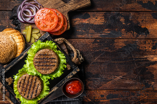 Cooking Plant based meatless burgers with vegetarian meat free roasted cutlets, patties, tomato and onion in a wooden serving tray. Wooden background. Top view. Copy space