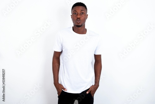 Portrait of lovely funny young handsome man wearing white T-shirt over white background sending air kiss