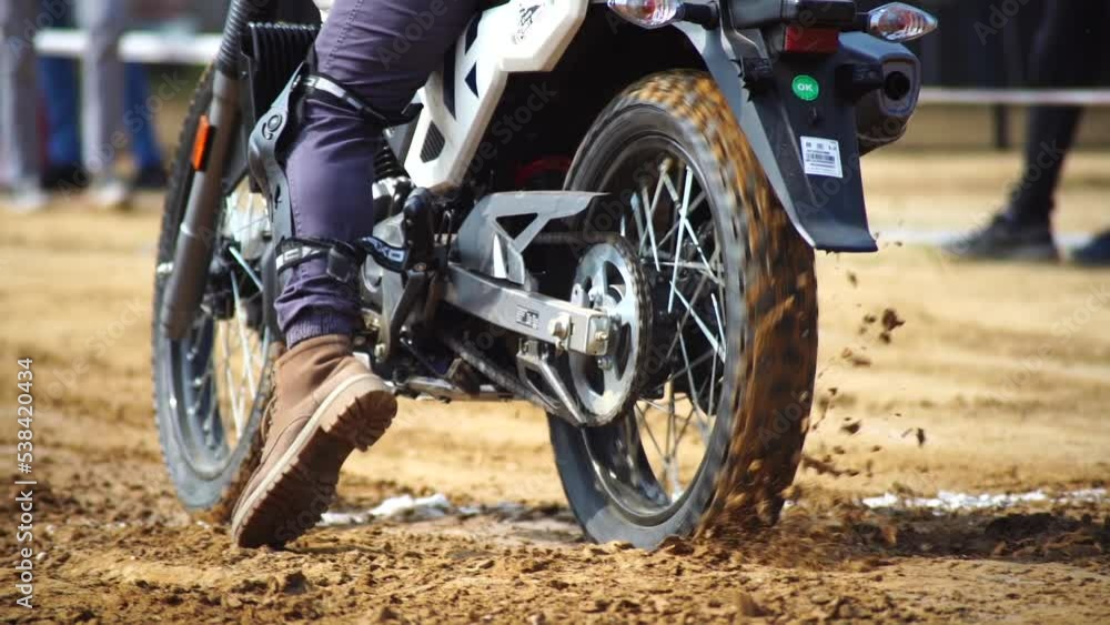 slow motion low to ground shot of ribbed tyre of off road motorcycle bike starting off on race throwing mud all over also shows protective gear of rider with boots, shin guards slow motion low to ground shot of ribbed tyre of off road motorcycle bike starting off on race throwing mud all over also shows protective gear of rider with boots, shin guards