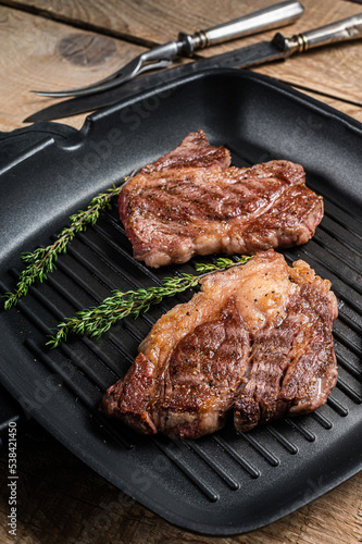 Grilled Chuck eye Roll beef steaks with herbs on grill skillet. Wooden background. Top view