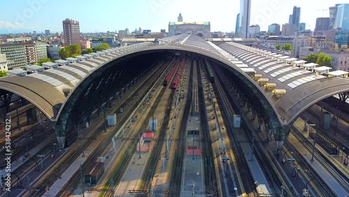 Aerial view of the station. Trains arrive at the station. An old wide arched structure of metal and glass above the station pillars. Tourism. Skyline with tall buildings. Italy, Milan, June 2022 photo