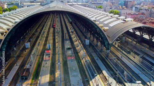 Aerial view of the station. Trains arrive at the station. An old wide arched structure of metal and glass above the station pillars. Tourism. Skyline with tall buildings. Italy, Milan, June 2022 photo