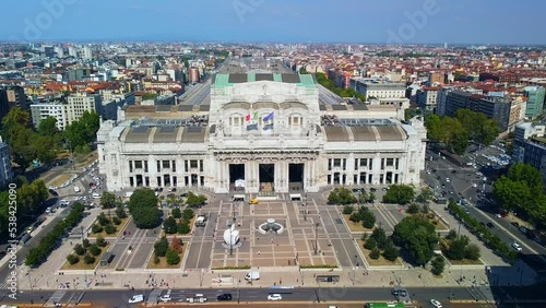 Aerial view of the station. Trains arrive at the station. An old wide arched structure of metal and glass above the station pillars. Tourism. Skyline with tall buildings. Italy, Milan, June 2022 photo