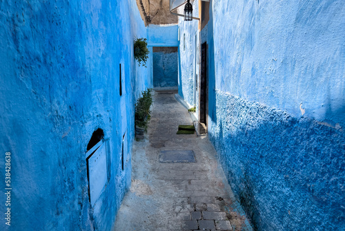 An empty narrow street with blue buildings in Chefchaouen © Hamza