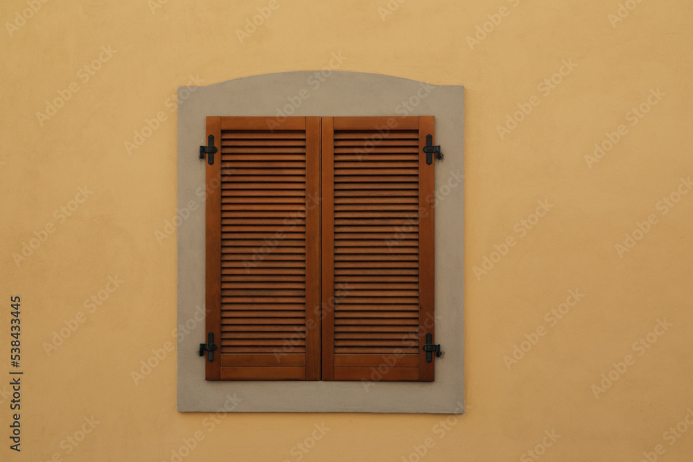 Yellow painted haus wall with a window with closed wooden shutter, no person