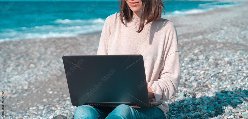 Girl in a hat works on a laptop on the beach,  seashore.