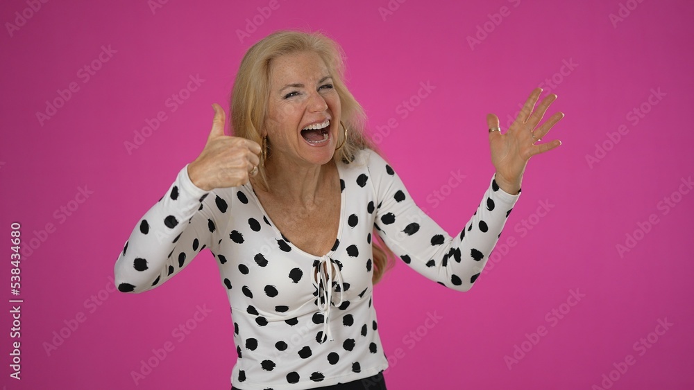 Excited surprised happy blonde woman 50s gives thumbs up wearing casual shirt isolated on solid pink background studio portrait Excited surprised happy blonde woman 50s gives thumbs up wearing casual shirt isolated on solid pink background studio portrait
