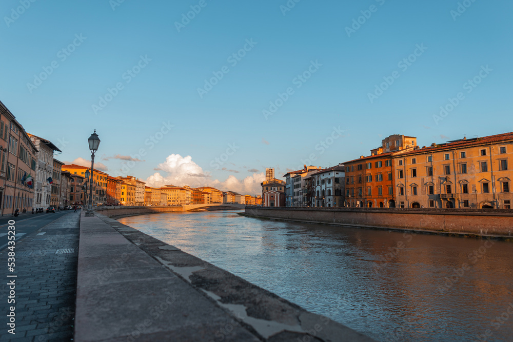 Beautiful vintage cozy European town with a river, bridge and colorful amazing creative houses at sunset in Pisa, Italy