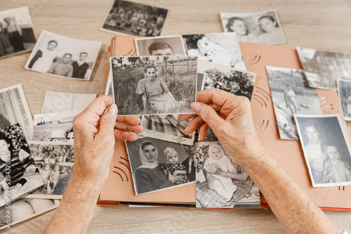 Senior woman is looking her own old photos at home. Elderly woman has got smile while remembering how young and beatiful she was. Selective focus. Photo was taken in 1953