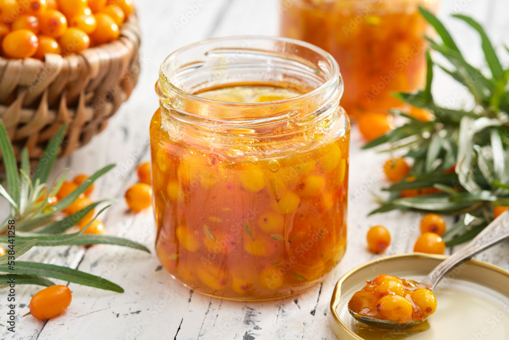 Jar of healthy sea buckthorn jam. Basket of ripe sea buckthorn berries on background. A spoonful of sea buckthorn jam in the foreground. Jar of healthy sea buckthorn jam. Basket of ripe sea buckthorn berries on background. A spoonful of sea buckthorn jam in the foreground.