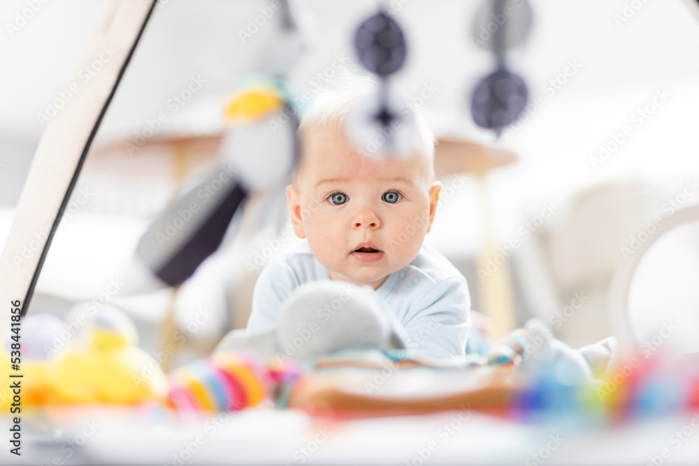 Cute baby boy playing with hanging toys arch on mat at home Baby activity and play center for early infant development. Baby playing at home Cute baby boy playing with hanging toys arch on mat at home Baby activity and play center for early infant development. Baby playing at home