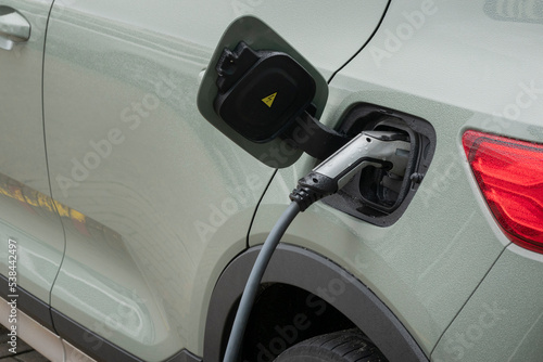 Close up of power supply plugged into gray electric car being charged. Power supply for electric car charging. Electric car charging station in the city