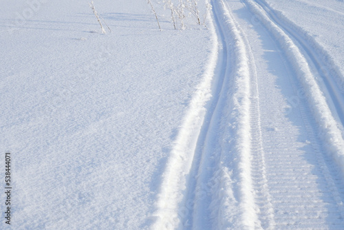 Track of traces from a snowmobile in drifts of white snow. Nature and outdoor on a winter sunny day. Background or wallpaper with snowy field © Deacon docs