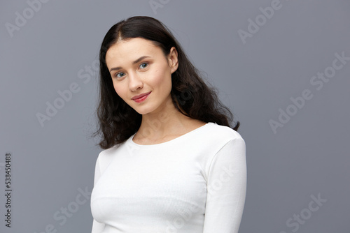a gentle woman stands full-face on a dark background in a tight white T-shirt, calmly lowered her hands down and looks forward smiling sweetly