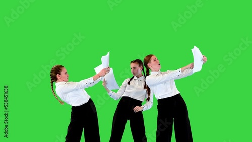 Young caucasian ladies in stage costumes pantomime with sheets of paper, then throw them away and start dancing on a Green Screen, Chroma Key. photo