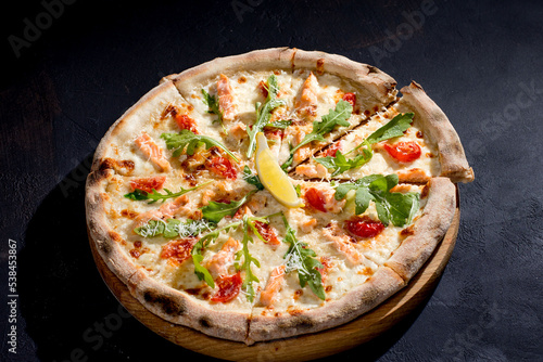 Pizza with salmon, mozzarella, cherry tomatoes, arugula, lemon and parmesan. Italian cuisine
