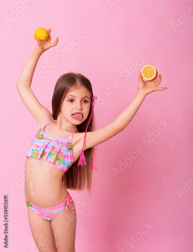 Caucasian beautiful little girl with fresh yellow lemons on a pink background. Little girl with lemon. Funny child isolated on pink.