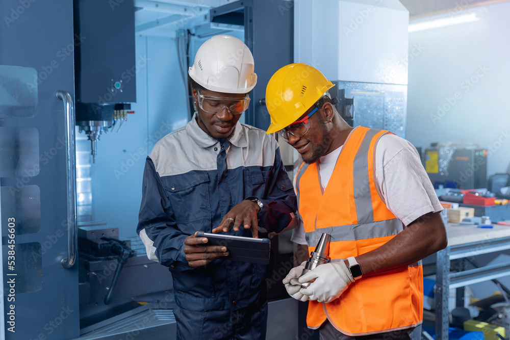 Team african american engineer in uniform using tablet computer for control CNC machinery on industry car factory Team african american engineer in uniform using tablet computer for control CNC machinery on industry car factory