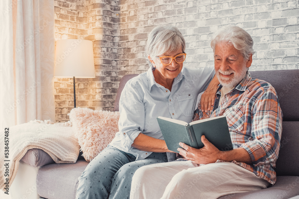 Portrait of couple of two cute grandparents reading a book together sitting on the sofa. Grandmother and grandfather relaxing weekend on free time. Portrait of couple of two cute grandparents reading a book together sitting on the sofa. Grandmother and grandfather relaxing weekend on free time.