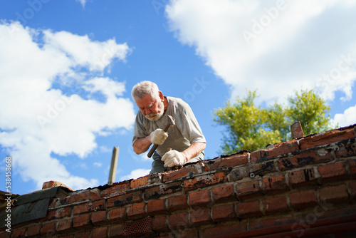 an elderly man dismantles the old brickwork and lays new bricks on the roof.