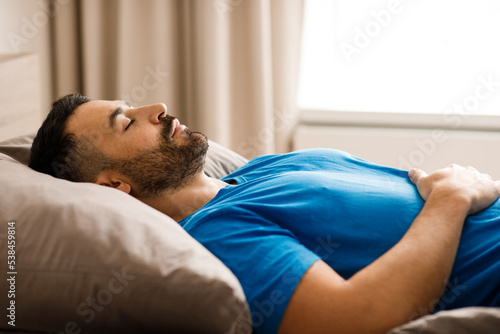 A relaxed millennial man of oriental appearance sleeps lying down with his eyes closed in the bedroom at home. Healthy sleep concept. side view