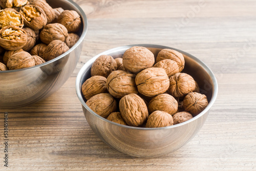 Newly harvested walnuts, designed in stainless steel bowls, on a wooden table,conceptual image