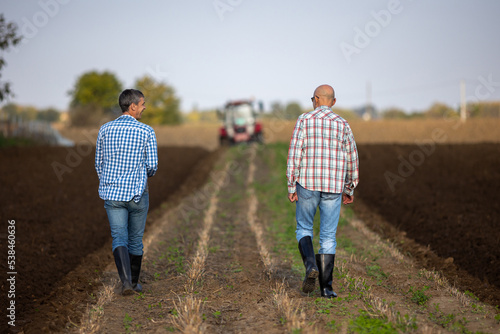 Farmers walking and talking in field with tractor in background