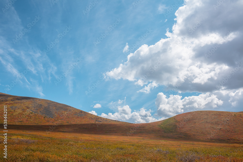Motley autumn mountain landscape with sunlit hill tops under cloudy sky. Vivid autumn colors in mountains. Cirrus clouds above multicolor hills. Sunlight and shadows of clouds in changeable weather. Motley autumn mountain landscape with sunlit hill tops under cloudy sky. Vivid autumn colors in mountains. Cirrus clouds above multicolor hills. Sunlight and shadows of clouds in changeable weather.