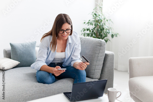 Shopping online at home. Happy woman paying by credit card for delivery order and purchases. Girl buying insurance with laptop and smartphone. Technology lifestyle for young investors, e-commerce