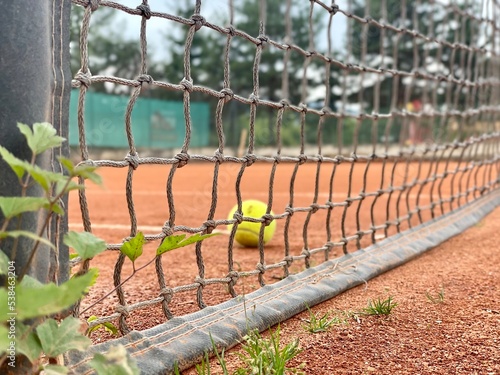 Dirty lonely tennis ball by the net at clay tennis court. After practice. Close up.