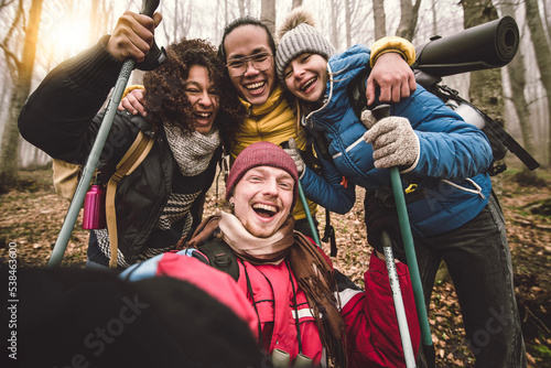 Multiracial happy friends with backpacks hiking in the forest - Group of young people taking selfie picture on the mountains - Travel, friendship and weekend activities concept