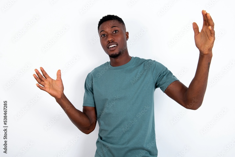 Cheerful young handsome man wearing green T-shirt over white background making a welcome gesture raising arms over head. Cheerful young handsome man wearing green T-shirt over white background making a welcome gesture raising arms over head.