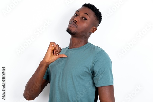 Closeup of cheerful young handsome man wearing green T-shirt over white background looks joyful, satisfied and confident, points at himself with thumb.