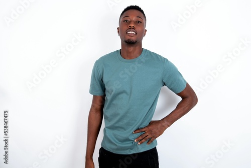 Studio shot of cheerful young handsome man wearing green T-shirt over white background keeps hand on hip, smiles broadly. © Jihan