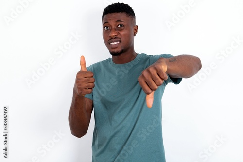 Obraz na plátne young handsome man wearing green T-shirt over white background feeling unsure making good bad sign