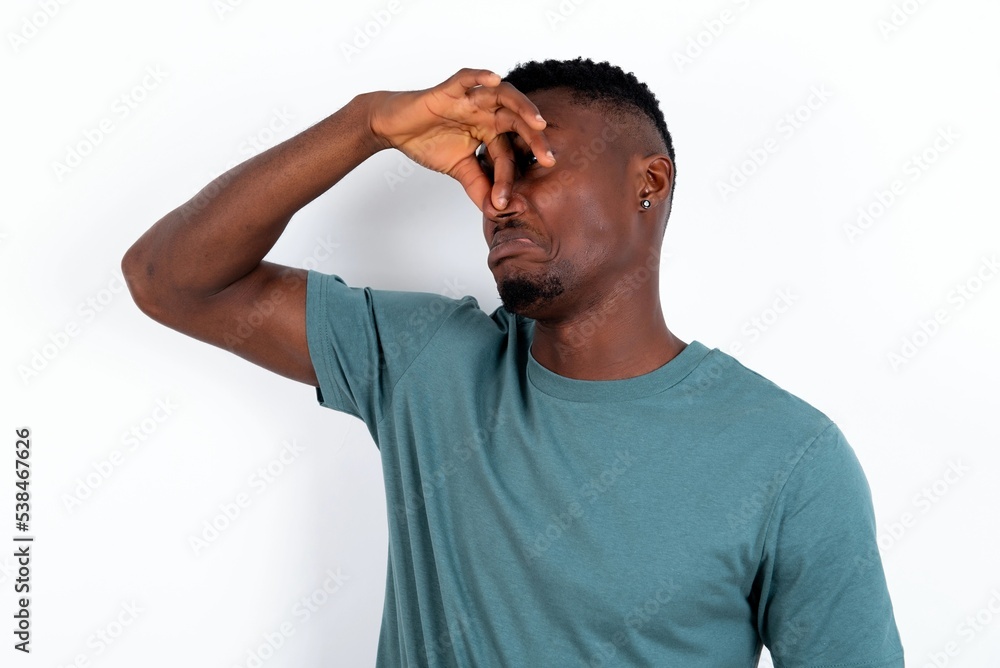 Displeased young handsome man wearing green T-shirt over white background plugs nose as smells something stink and unpleasant, feels aversion, hates disgusting scent. Displeased young handsome man wearing green T-shirt over white background plugs nose as smells something stink and unpleasant, feels aversion, hates disgusting scent.
