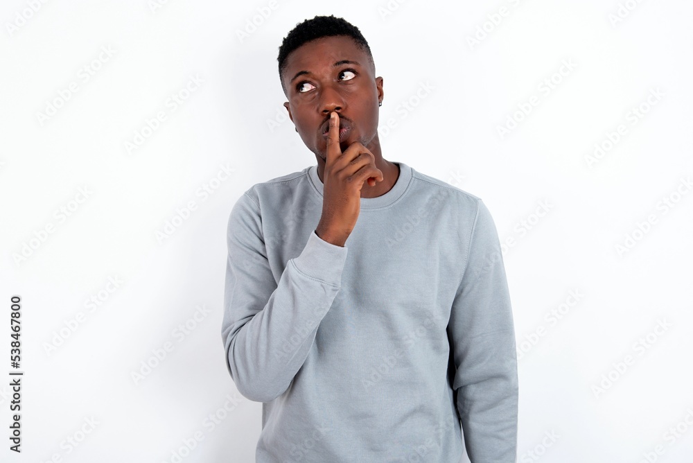 young handsome man wearing grey sweater over white background silence gesture keeps index finger to lips makes hush sign. Asks not to share secret young handsome man wearing grey sweater over white background silence gesture keeps index finger to lips makes hush sign. Asks not to share secret