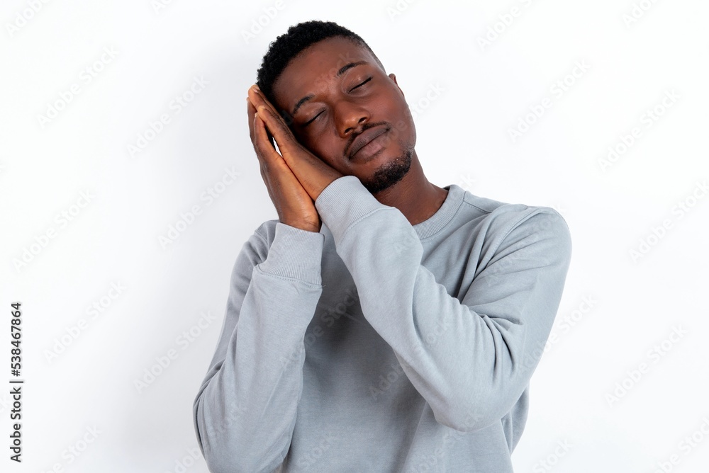 young handsome man wearing grey sweater over white background leans on pressed palms closes eyes and has pleasant smile dreams about something young handsome man wearing grey sweater over white background leans on pressed palms closes eyes and has pleasant smile dreams about something