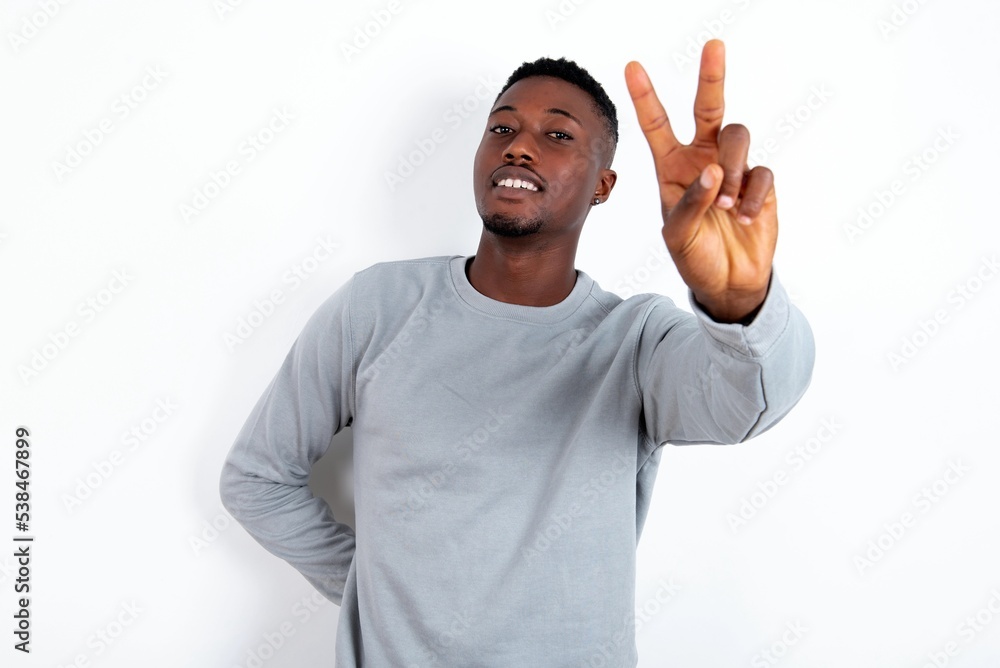 young handsome man wearing grey sweater over white background smiling and looking happy, carefree and positive, gesturing victory or peace with one hand young handsome man wearing grey sweater over white background smiling and looking happy, carefree and positive, gesturing victory or peace with one hand