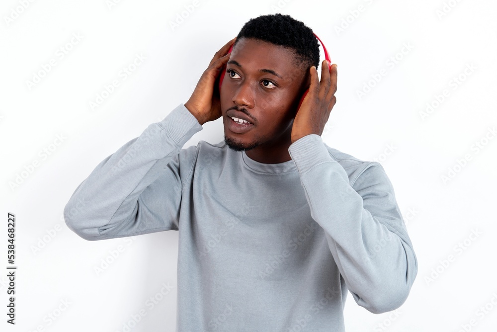 young handsome man wearing grey sweater over white background wears stereo headphones listens music concentrated aside. People hobby lifestyle concept young handsome man wearing grey sweater over white background wears stereo headphones listens music concentrated aside. People hobby lifestyle concept