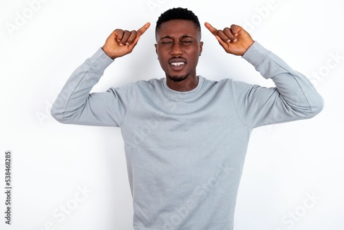 Photo of crazy young handsome man wearing grey sweater over white background screaming and pointing with fingers at hair closed eyes